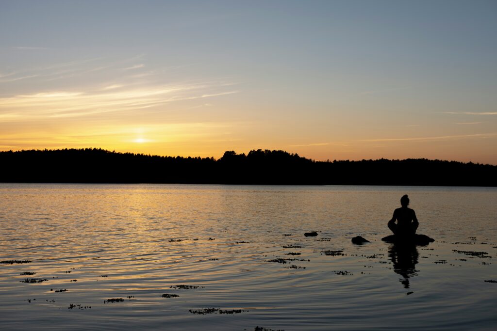 Person meditating outdoors at sunrise to reduce stress naturally